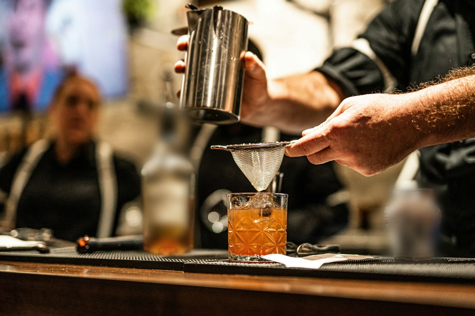 Bartender straining a cocktail into a rocks glass on a bar top