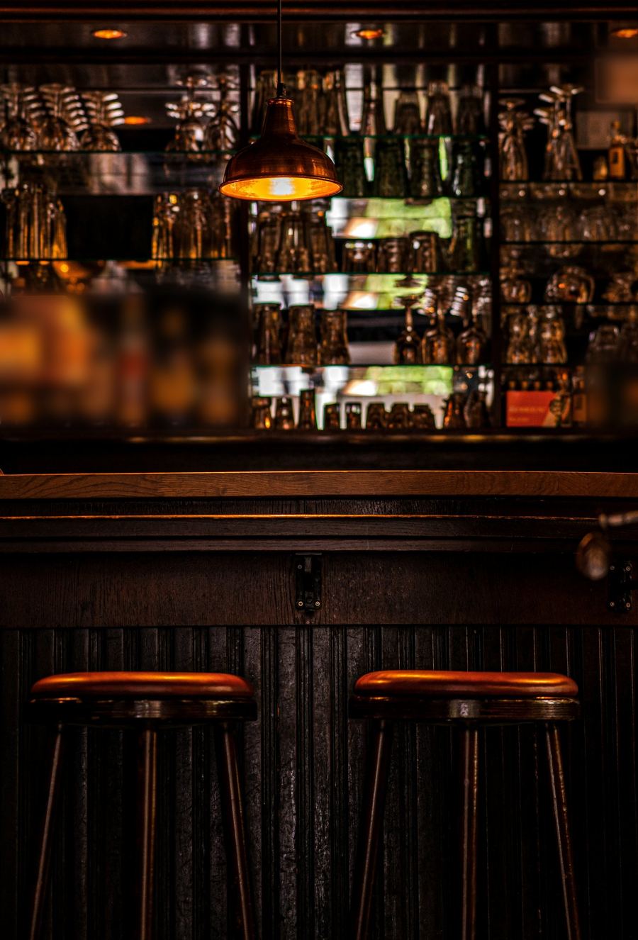 Neighborhood bar with a copper pendant lamp, glass shelves, and two wooden bar stools